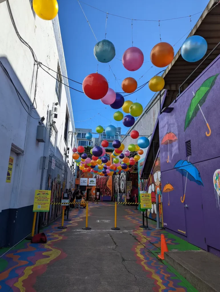 Ruelle avec ballons colorés, peintures au sol et fresque murale avec parapluies, à visiter si vous êtes à San Francisco.