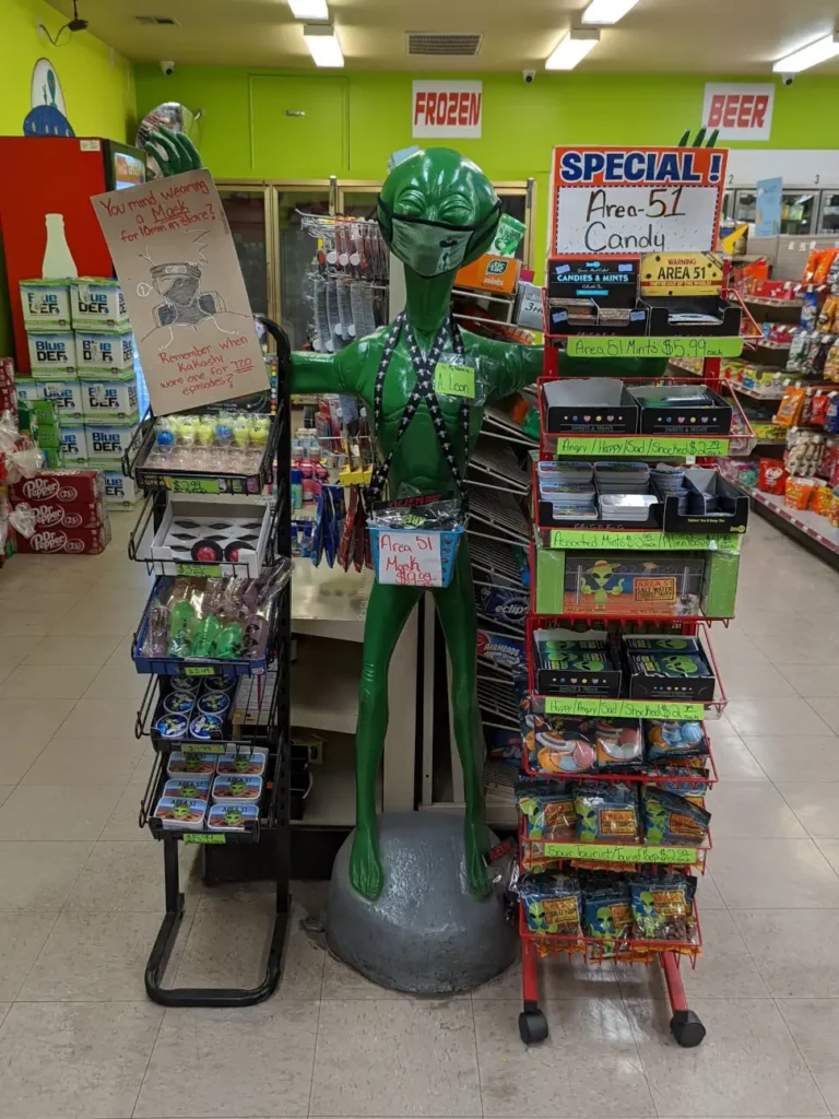 Statue d’un alien situé en tête de gondole. Il porte un masque et promeut des produits, tels que des bonbons de la Zone 51.