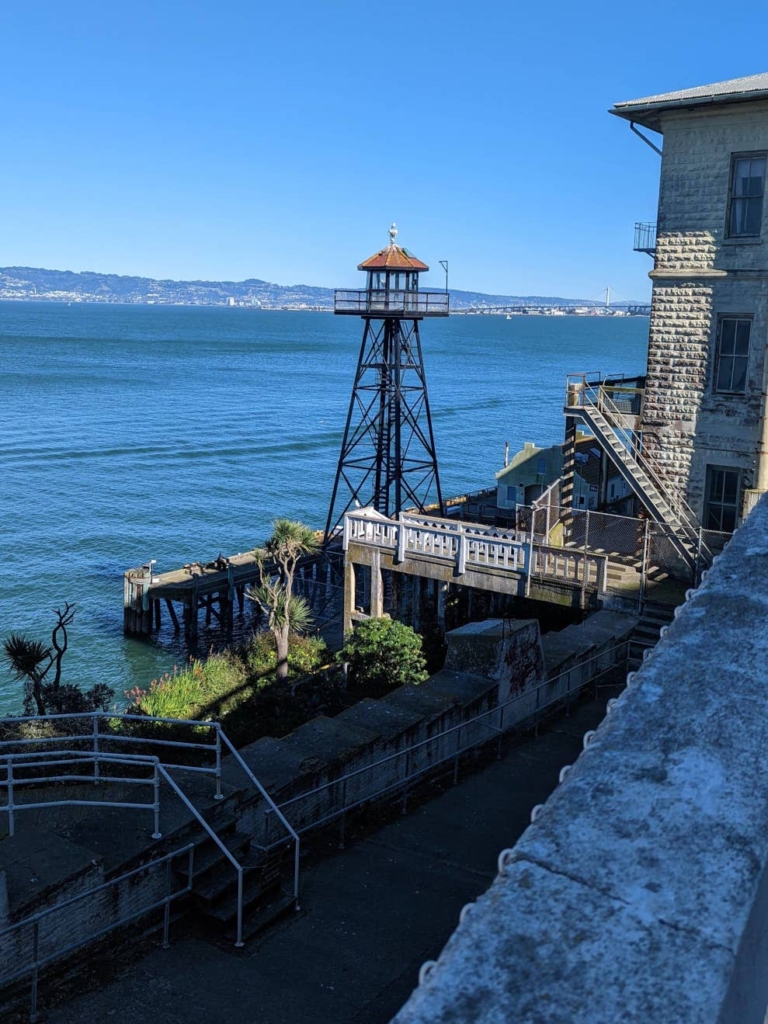 Vue en plongée sur la Tour de Garde et les eaux de la baie de San Francisco. On observe également des escaliers ainsi qu’un ponton en bois.