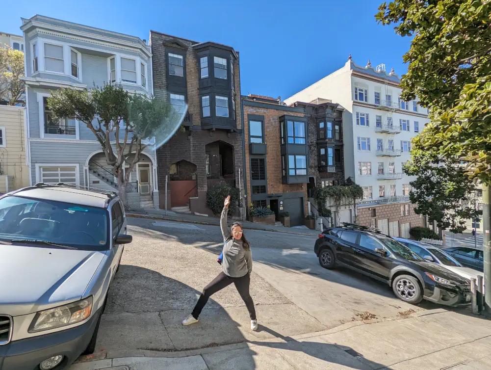 Hélo qui pose devant une maison victorienne, dans Lombard Street. Elle est moderne, avec un mélange de briques marron et de fenêtres en métal noires.