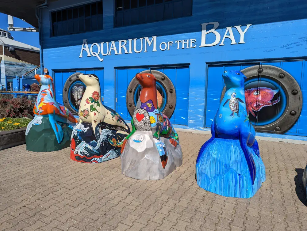 Devanture bleue de l’Aquarium of the Bay de San Francisco, au Pier 39. Devant se trouvent 4 statues d’otaries avec motifs.