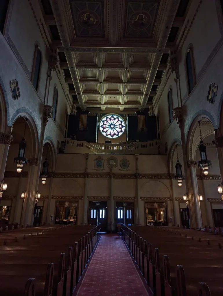 Intérieur sombre de l'église Saints Peter and Paul Church, dont l’allée centrale est éclairée par une rosace lumineuse.