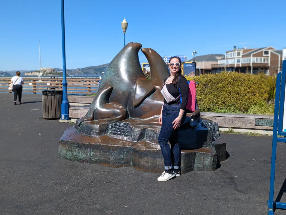 Hélo pose avec le sourire devant la statue en bronze d'une famille d'otaries, située au Pier 39 à San Francisco.