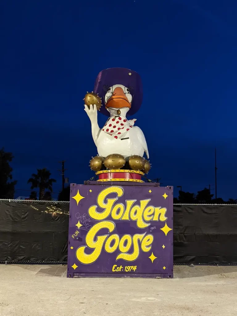 Sculpture d’un canard blanc, portant un chapeau violet. Il est posé sur un cube violet, sur lequel est écrit “Golden Goose Est 1974”.