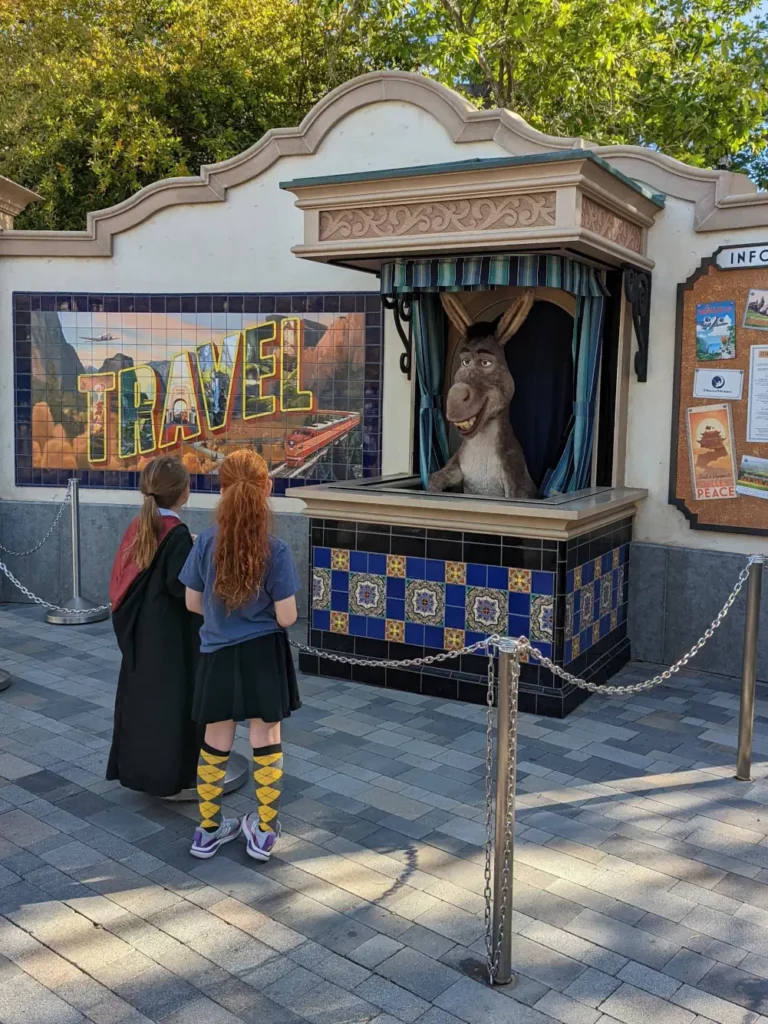 Deux enfants se tiennent debout derrière une rambarde, devant un animatronique de l’âne de Shrek.