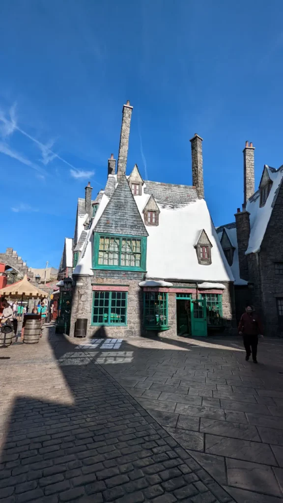 Façade principale du magasin de confiserie “Honeydukes”. Sur son grand toit se trouve de la neige.