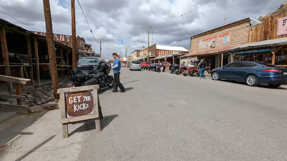 Oatman Highway traversant le village minier. Sur le bord de la route se trouve un panneau en bois indiquant “Get yer kicks”.