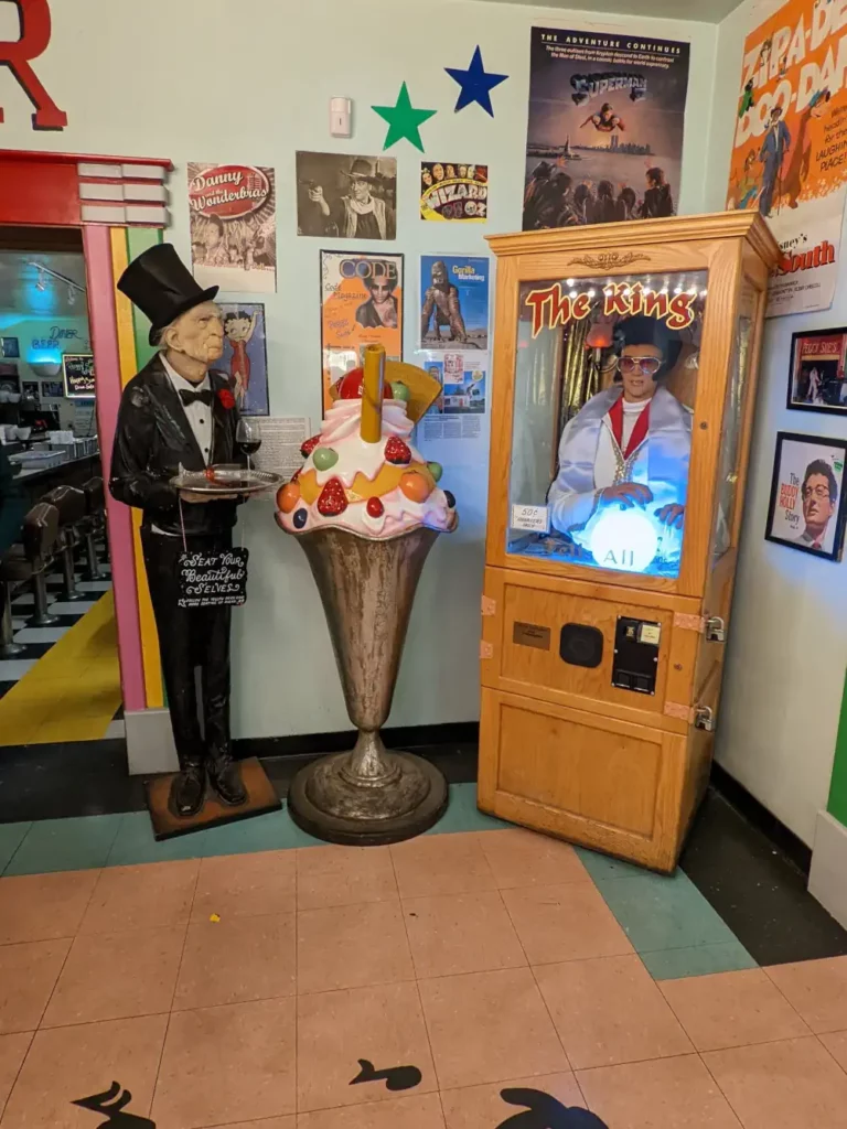 Entrée du restaurant Peggy Sue's 50's Diner, où se trouvent les statues d’un vieux majordome et d’une glace géante, ainsi que la fortune telling machine “The King”.