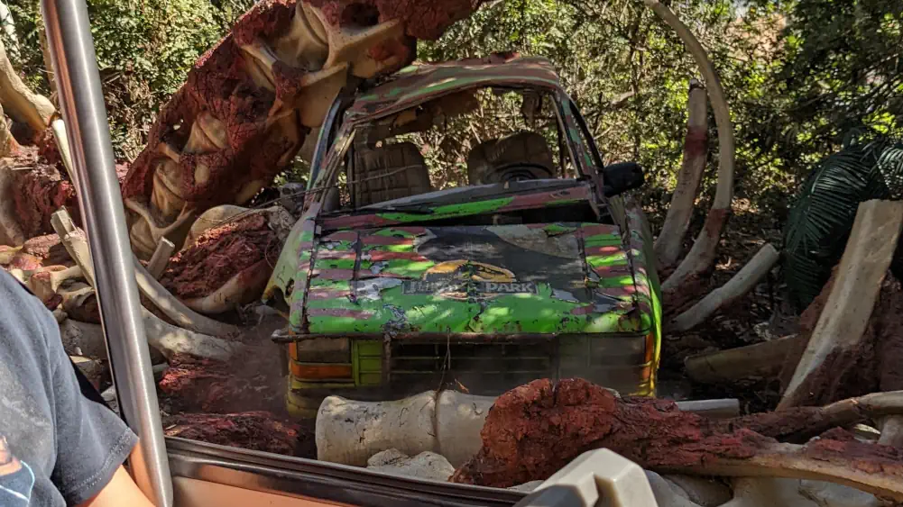 Voiture verte de Jurassic Park, écrasée par un os géant de dinosaure. Il ressemble à une colonne vertébrale.