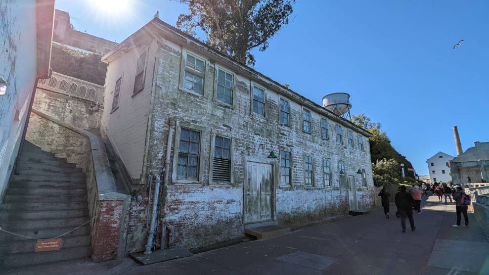 Vieux bâtiment à la façade usée. Derrière se trouve le château d’eau. Au loin se trouve le quartier-maître.