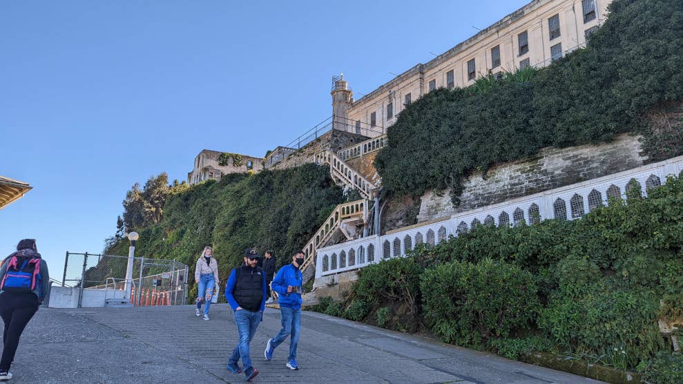 Vue en contre plongée sur la prison d’Alcatraz, le phare et la maison du gardien. Pour y accéder, il faut emprunter un escalier à travers la verdure.