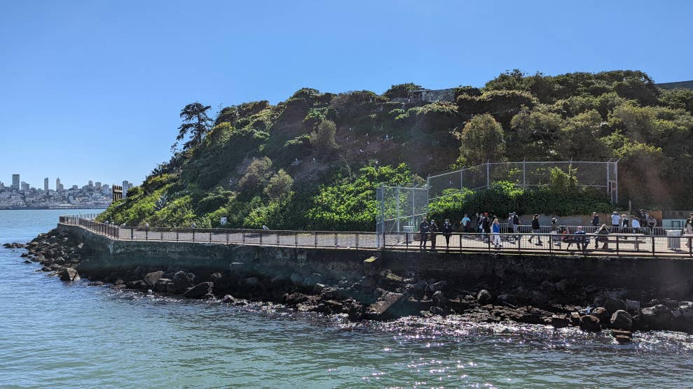 Extrémité de la zone d’embarquement de l’île d’Alcatraz, à bord d’un ferry. On y voit des touristes qui marchent, de la végétation et des oiseaux.