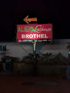 Panneau rouge indiquant, en lettres vertes et blanches : “ALIEN Cathouse BROTHEL”. Au-dessus se trouve une flèche orange.