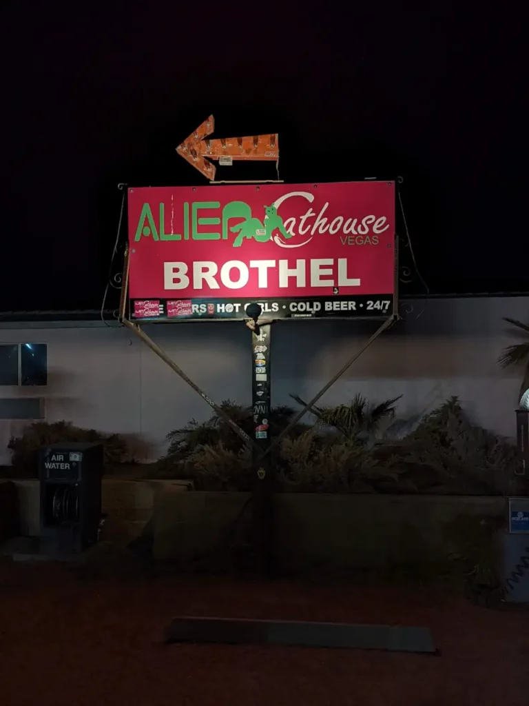 Panneau rouge indiquant, en lettres vertes et blanches : “ALIEN Cathouse BROTHEL”. Au-dessus se trouve une flèche orange.