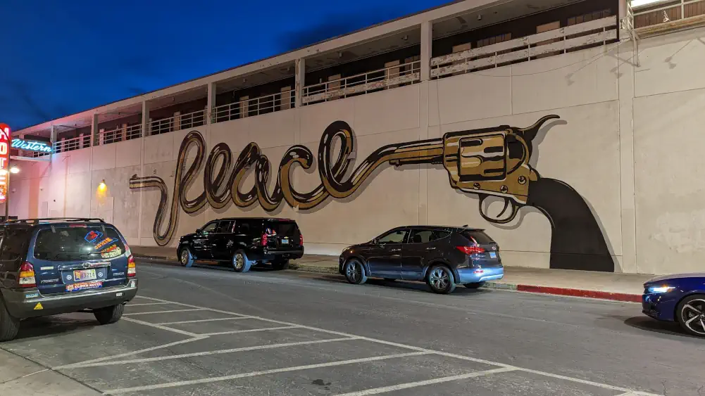 Peinture murale dorée et noire, dans une rue perpendiculaire à Fremont Street. Les lettres “PEACE” sortent d’un pistolet.