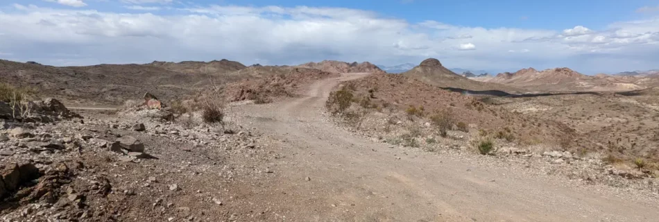 Route de terre déserte et rocailleuse survolée d’un ciel bleu, typique d’un road trip sur la cote ouest des USA.