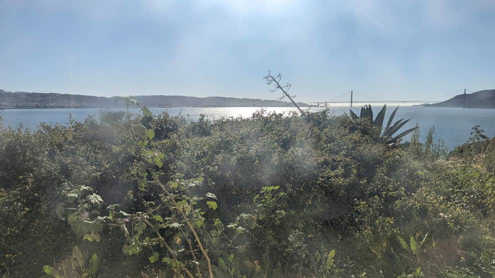 Vue à travers un hublot sale de la prison d’Alcatraz, débouchant sur de la végétation, la baie de San Francisco et le pont du Golden Gate.