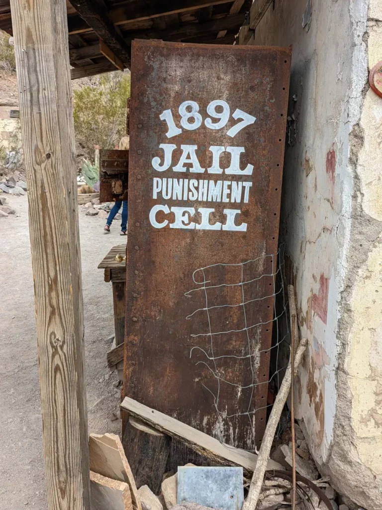 Côté d’une ancienne cellule de prison rouillée à Oatman. Il est écrit en lettres blanches “1897 Jail Punishment Cell”.