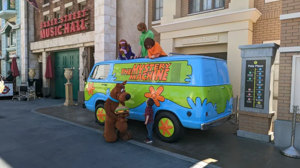 Van bleu, vert et orange de la “Machine Mystérieuse”, devant lequel Scooby Doo parle avec un enfant. Le reste de la bande se tient debout par le toit.