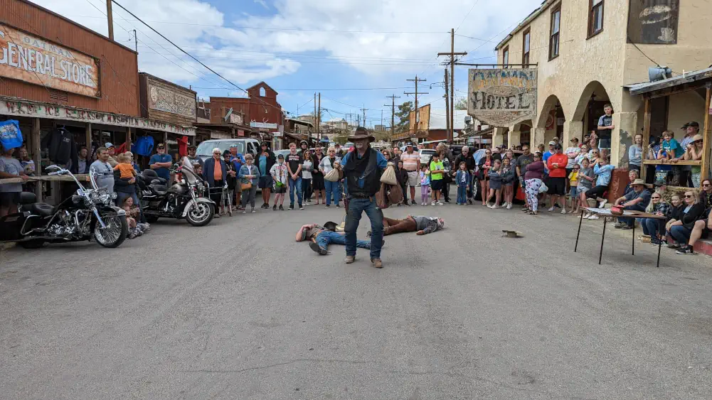 Un cow-boy se tient debout avec deux sacs blancs à la main. Deux hommes sont allongés par terre à côté de lui.