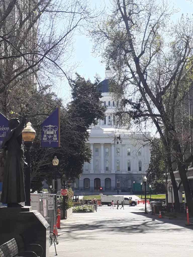 Façade blanche du Capitole de l'État de Californie situé à Sacramento, caché derrière les arbres du parc.