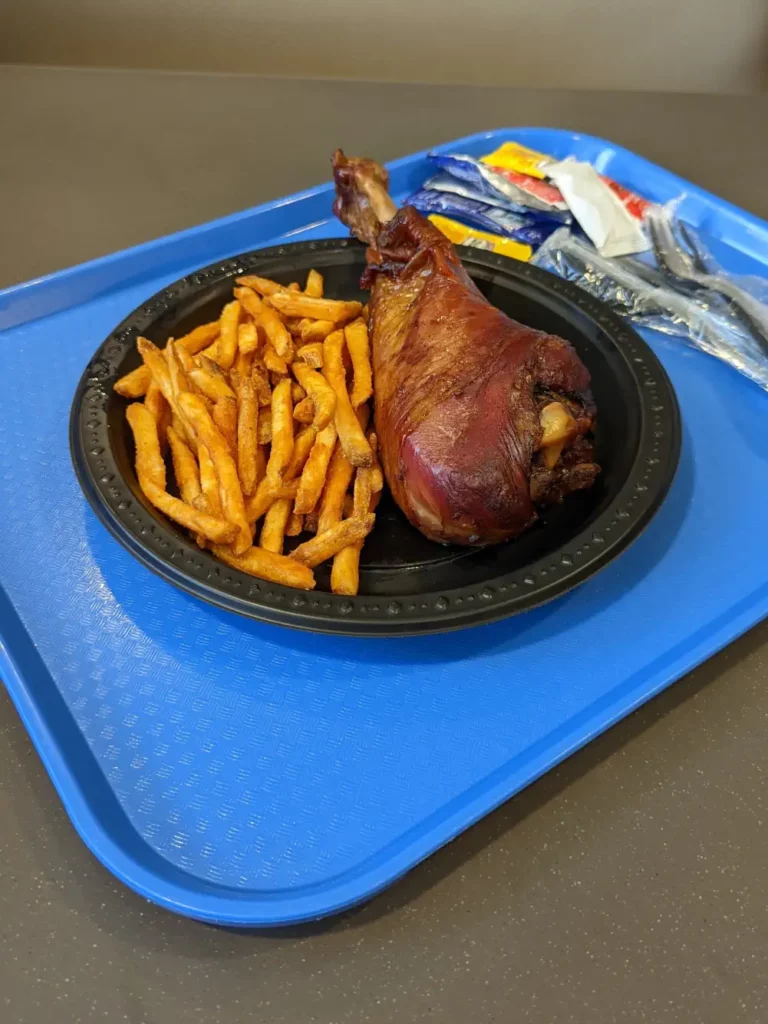 Assiette noire posée sur un plateau bleu. Elle contient un gros morceau de Famous Turkey Leg et des frites au paprika.