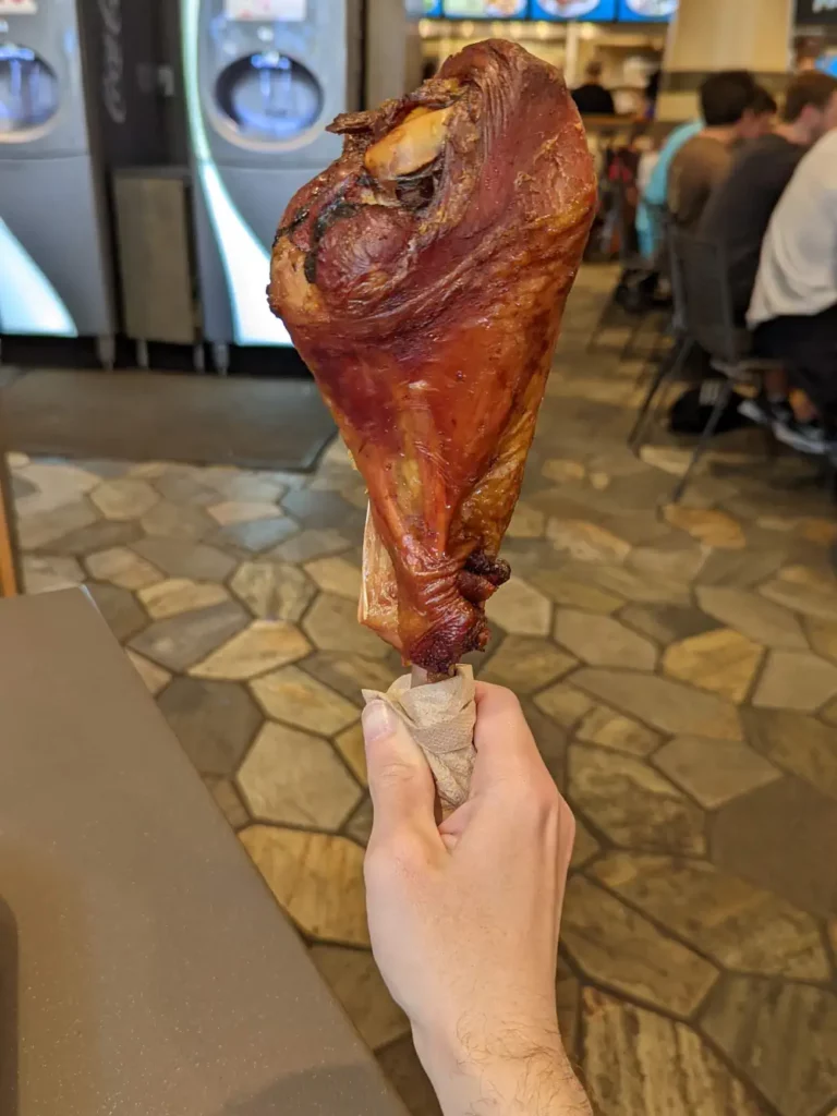 Nano tenant un Famous Turkey Leg. Le morceau est plus grand que sa main. On voit également un os qui dépasse.