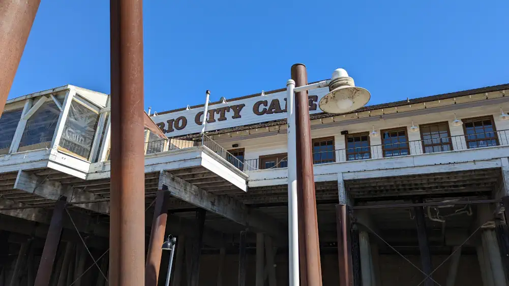 Contre-plongée sur le restaurant “Rio City Cafe”, situé sur un ponton en bois derrière des poteaux en métal industriels.