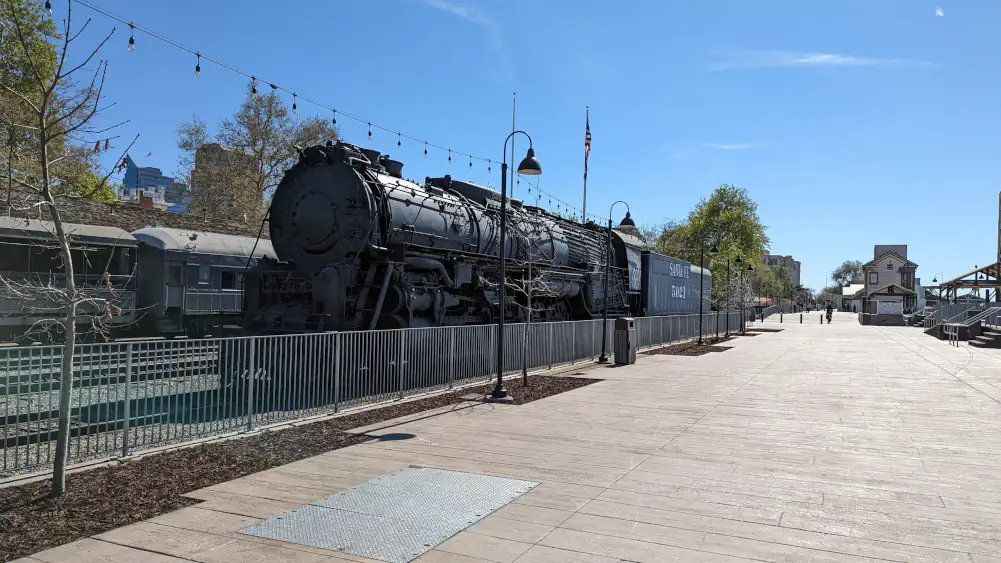 Vieux train locomotive noir “Santa Fe 5021”. Il se situe à côté d’une grande esplanade en bois.