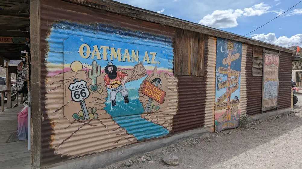 Façade d’un bâtiment à Oatman, recouvert de tôle et de 3 peintures. Sur l’une d’elle est écrit “Oatman, AZ. - Route 66”.