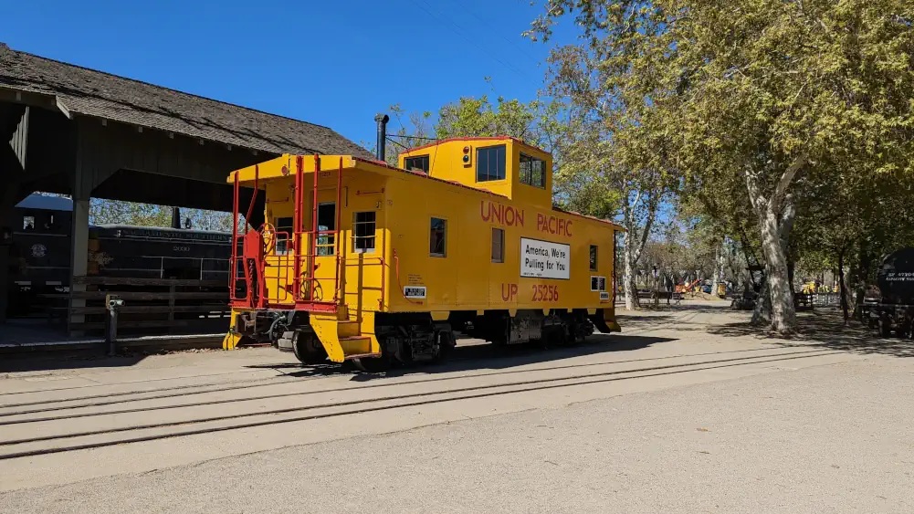 Fourgon-frein (ou wagon d’accompagnement) jaune et rouge du “Union Pacific UP 25256”. Il est écrit “America, We’re Pulling for You”.